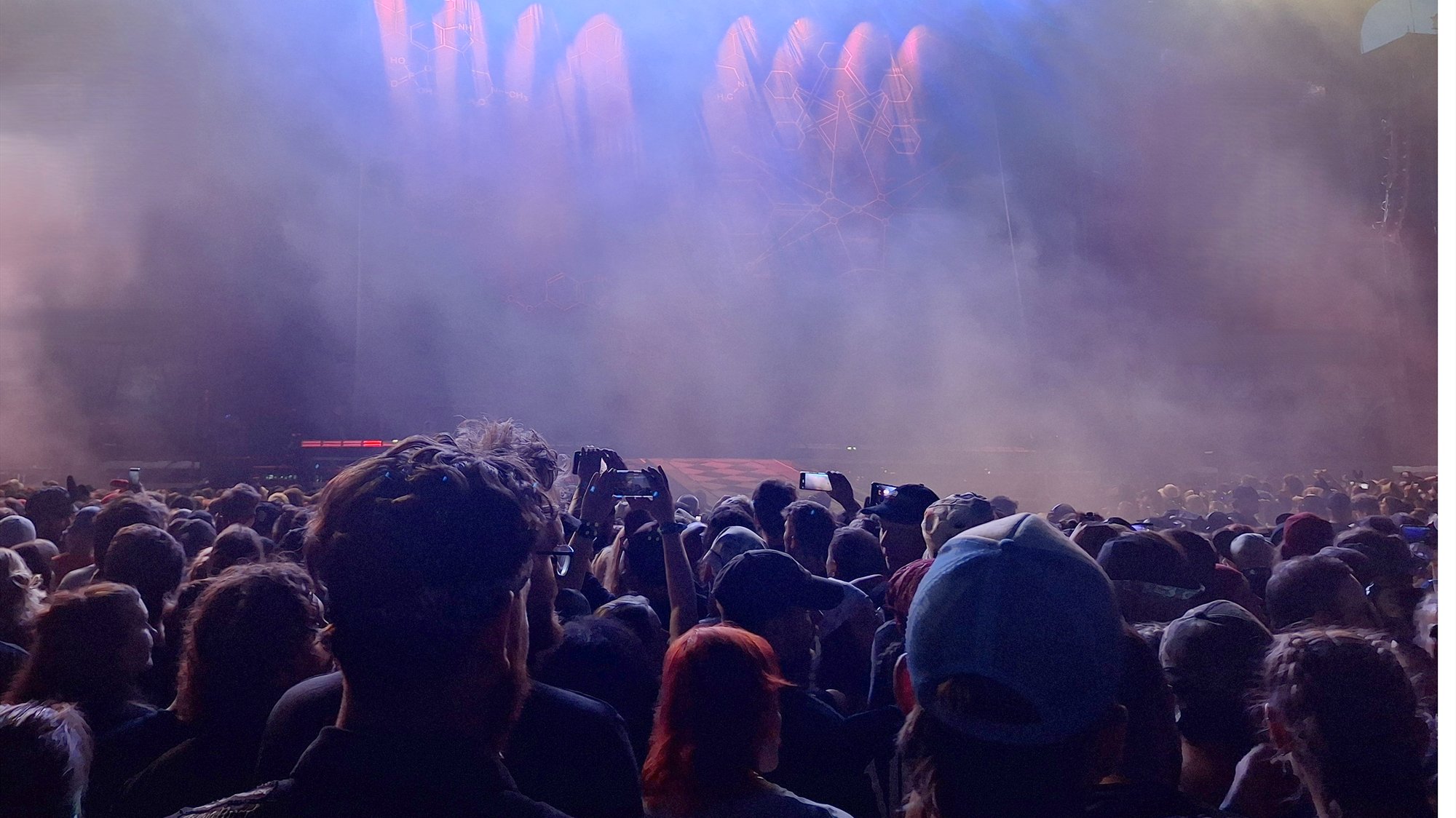 Publikum bei Nacht vor einer Festivalbühne, Scheinwerferlicht und Bühnennebel über den Köpfen.