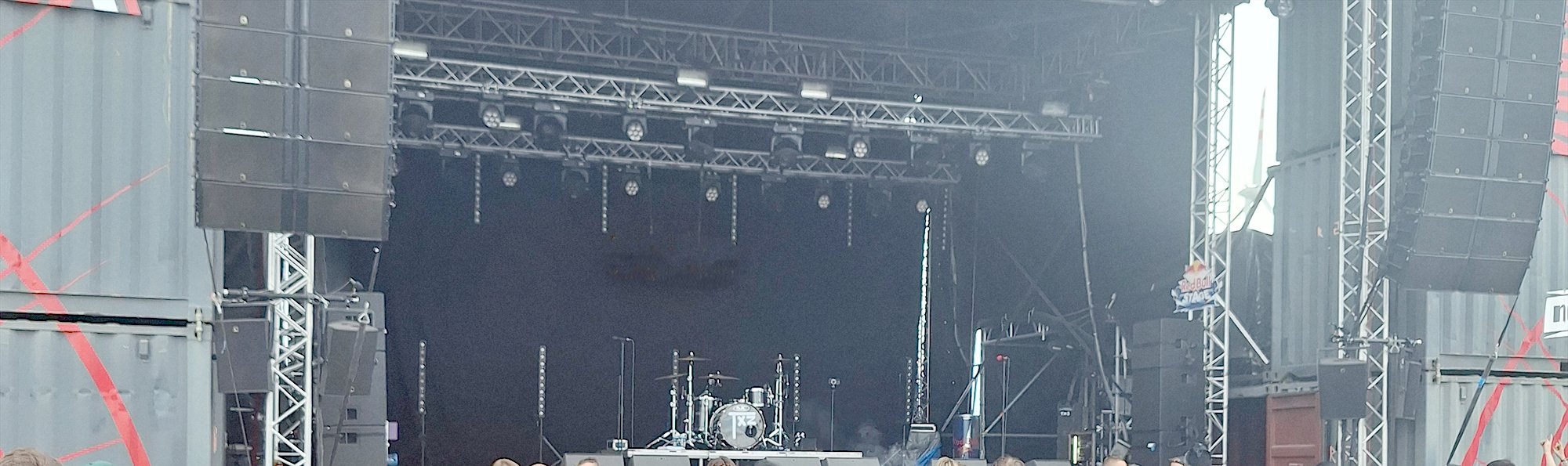 Festivalbühne bei Tag mit hohen Lautsprechertürmen und Traversen, davor die Hinterköpfe des Publikums.